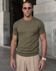 Man wearing olive green knit t-shirt by a stone wall, Morengar summer menswear