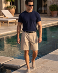 Man in navy knit t-shirt and beige shorts walking by the pool